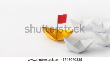 Leadership concept. Red flag Origami Yellow Paper boat (ship) leading the other white boats.  One leader ship leads other ships.
 Royalty-Free Stock Photo #1746090335