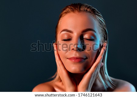 Attractive young girl touching face.  Photo of a blonde girl with perfect skin on a gray background. The concept of beauty and skin care.