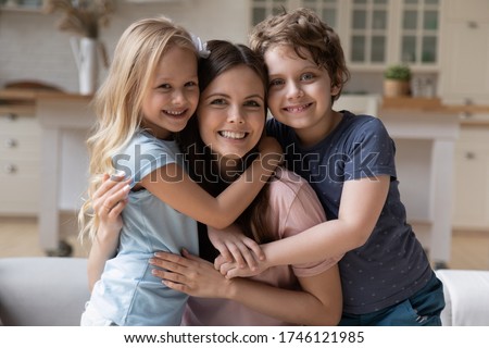 Portrait of happy young mother hug cuddle with smiling little children relax on weekend at home, smiling overjoyed small kids embrace mom or nanny show love and gratitude, family bonding concept Royalty-Free Stock Photo #1746121985