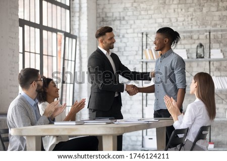 Smiling executive congratulating successful African American employee with promotion, shaking hands at corporate meeting, confident team leader greeting new member at briefing in boardroom Royalty-Free Stock Photo #1746124211