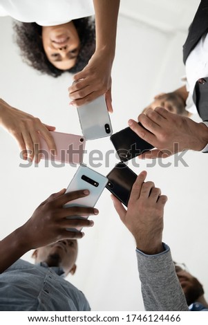 Close up bottom view diverse people using phones, standing in circle, employees holding smartphones in hands, looking down at screen, social media addiction, chatting, shooting video or photo