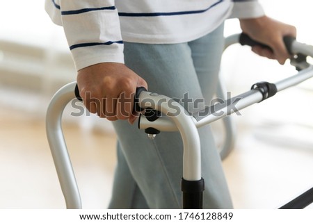 Close up view hands of old disabled woman holding walking frame makes exercises regain leg strength after operation, injury, accident. Safe design equipment, part of rehabilitation programme concept Royalty-Free Stock Photo #1746128849