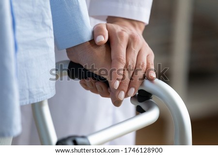 Physiotherapist touches disabled elderly woman hand while she holding walking frame close up view. Nurse supporting patient during exercise rehabilitation therapy. Caregiving, help, eldercare concept Royalty-Free Stock Photo #1746128900