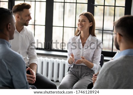 Confident smiling woman coach speaking at meeting, happy diverse people sitting in circle at group therapy session with psychologist, mentor training staff, team building activity in office Royalty-Free Stock Photo #1746128924