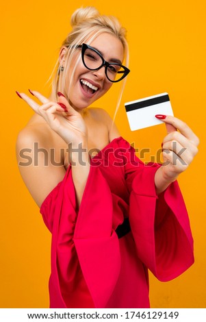 attractive girl in a red dress holds a credit card with a layout for the bank on a yellow background