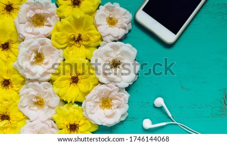 Beautiful summer background with fresh roses, smartphone and white earphones on an old painted wooden table for blogs, web design, posters, seasonal cards and business concepts