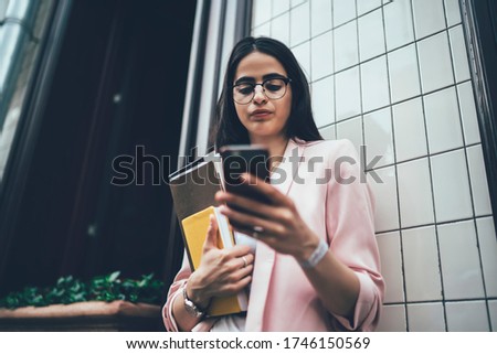 Millennial student with textbook using 4g internet connection for doing online banking and make payment for web education courses, hipster girl in glasses reading publication on university website