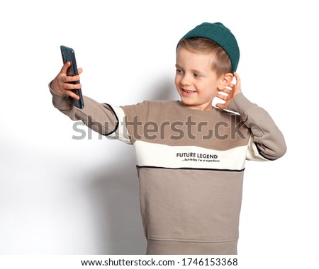 A child takes a selfie on a smartphone. A beautiful European boy with blue eyes is photographed on the phone, smiling, posing. Modelman. Gadgets, cellular communications, Internet, telephony.