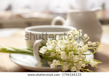 Cup of coffee on a saucer with lilies of the valley