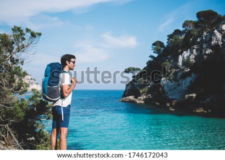 South Asian wanderlust with rucksack enjoying summer vacations for explore wild nature at coastline,Indian male in sunglasses enjoying travel active recreating during solo holidays on Balearic islands Royalty-Free Stock Photo #1746172043