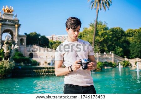 Serious caucasian male photographer amateur checking settings on camera spending free time explore city destinations, pensive hipster guy traveler visiting town on summer vacations on sunny day