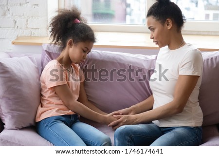 African mother school age daughter hold hands sit on couch having confidential conversation mom encourages supports little kid girl in her little problems or telling about separation with dad concept. Royalty-Free Stock Photo #1746174641