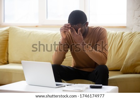 African guy sit on couch in front of pc takes off glasses rubs eyes feels tired by long time usage of laptop. Frustrated upset man received bad news looking worried thinking ponders decision concept Royalty-Free Stock Photo #1746174977