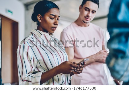 Dark skinned woman using modern smartphone device for search web publication during meeting with friends, diverse hipster girl with cellular installing app for making online booking and banking