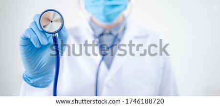 Healthcare and medical check up concept. Male Asian doctor holding stethoscope in hand. Physician man wearing surgical mask and gloves working in hospital clinic during Coronavirus (COVID-19) pandemic Royalty-Free Stock Photo #1746188720
