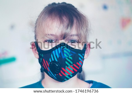 Portrait of a cute little girl eleven years old in a medical multi colored mask looking at camera, Corona virus, AVID-19, quarantine and stay home and  safe concept