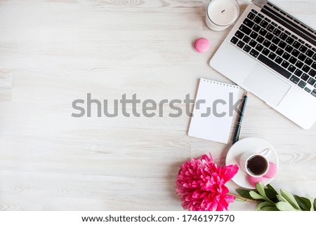 Banner with copy space - a blank notebook, pink peony flower, coffee cup, pen, sweet macarons and laptop, a light wooden background. To-do list, plans, dreams. Work from home. Top view.
