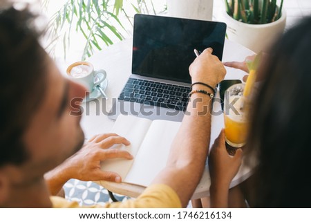 Cropped image on woman and man student learning together sitting at table in cafe interior cooperate on task, rear view of female and male cooperating on remote job meeting pointing on laptop computer