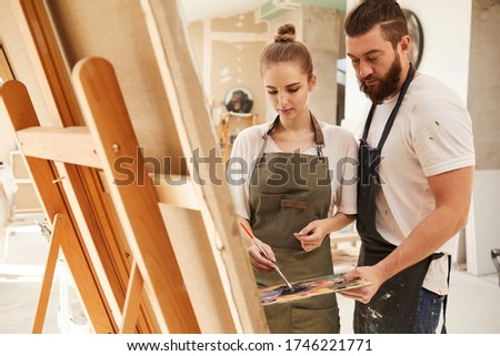 Warm toned portrait of creative couple painting picture together while standing by easel and holding palette, copy space
