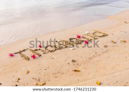 the word thailand on sand, exotic frangipani flowers on the seashore, paradise flowers plumeria, background picture with flowers by the ocean, yellow sand in Asia