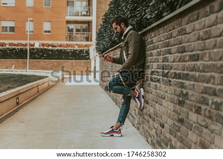 Serious , urban man looking at mobile phone while waiting leaned on the wall