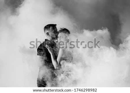 guy and a girl in black clothes hug inside a white smoke