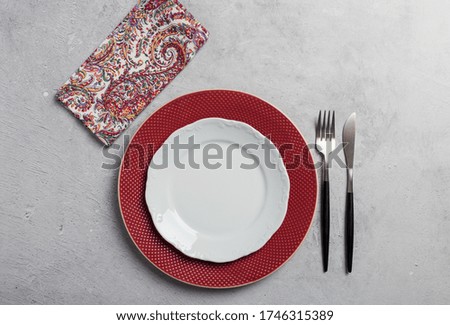 Simple minimal table setting with two dishes, silverware and napkin on gray concrete background. Concept of frame with empty serving plate, top view, flat lay, copy space