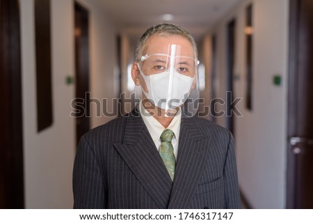 Mature Japanese businessman with mask and face shield in the corridor
