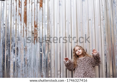 Stylish, fashionable girl with long hair posing on a background of gray metal. Portrait of happy baby. Place for text. Soft focus, retro photo.