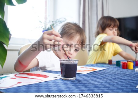 Children engaged in creativity in home interior. Child draws and colors the picture with paints and a brush. Developing activities and leisure during self-isolation and quarantine. Foreground focus