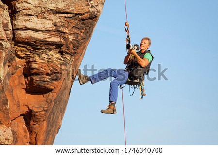 Rock climber taking pictures while hanging in front of a rock