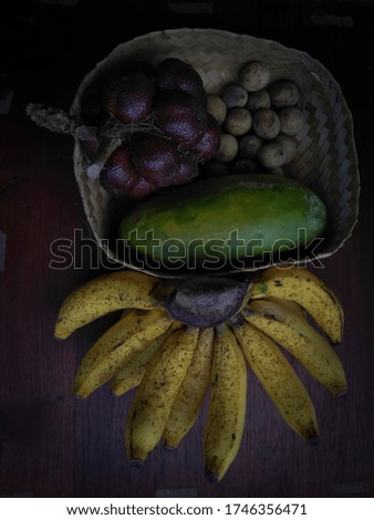 Bananas, papaya, salak, and duku on a brownish wooden table, a background concept or props about nutritious food.