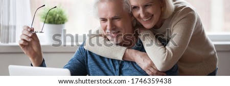 60s wife hug husband spouses looking at pc screen read good news. Make videocall talk with grownup children, receive great offer eyewear sale concept. Horizontal photo banner for website header design Royalty-Free Stock Photo #1746359438