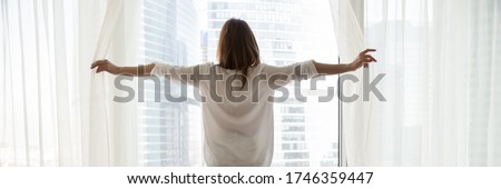 Rear back view woman opening white curtains enjoy cityscape modern skyscrapers buildings view and new day, happy homeowner, luxury lifestyle concept. Horizontal photo banner for website header design Royalty-Free Stock Photo #1746359447
