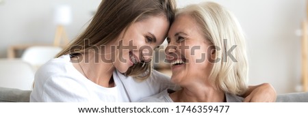 Grown up daughter cuddle old 60s mama happy excited women laughing seated on sofa in living room. Family bond, care and love concept. Horizontal photo close up banner for website header design concept