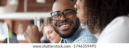 Diverse employees working in shared office focus on african guy flirting with female colleague, teammates friendly conversation good relation concept. Horizontal photo banner for website header design