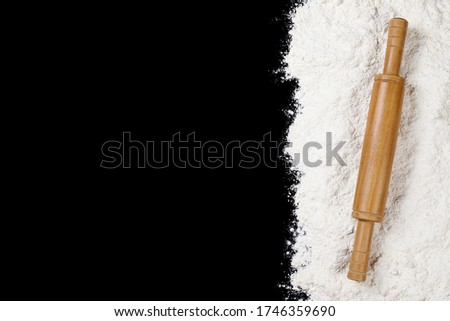 A pile of flour and roller pin on black background with copy space.
