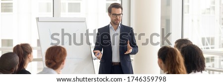 Speaker talking to audience makes presentation using flip chart interacts with group of staff employees, corporate seminar, training activity concept. Horizontal photo banner for website header design Royalty-Free Stock Photo #1746359798