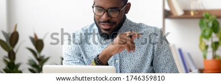 Millennial African employee sit at office desk using pc look at screen read e-mail, received good business news, entrepreneur do remote job from home, horizontal photo banner for website header design