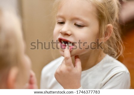 Child girl looks in the mirror at changing baby teeth in her mouth. Royalty-Free Stock Photo #1746377783