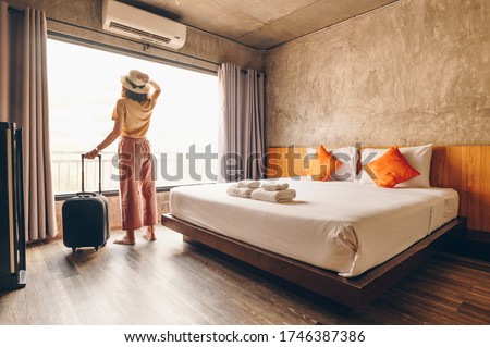 Portrait of tourist woman standing nearly window, looking to beautiful view with her luggage in hotel bedroom after check-in. Conceptual of woman lifestyle when traveling on her vacation. Royalty-Free Stock Photo #1746387386