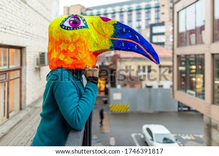 Masked woman - brightly colored bird head with a large beak leaning on the railing. homemade original costume for the holiday.