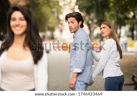 Jealousy. Jealous Girlfriend Calling Boyfriend Distracted By Other Attractive Woman Walking During Date In Park. Selective Focus Royalty-Free Stock Photo #1746423464