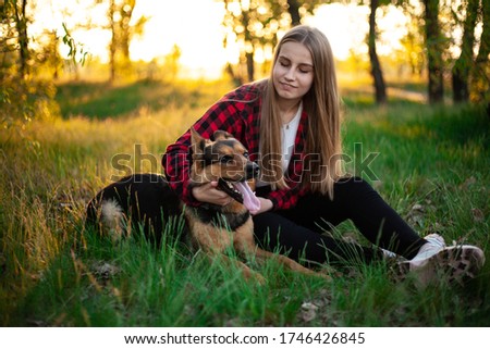 Happy blonde girl is played with a dog. Girl hugs a dog sitting on the grass. Dog Shepherd, female. Friend dog. Outdoor photo shoot at sunset
