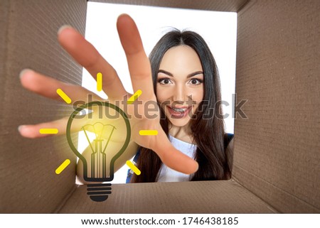 Happy girl opening postal package with light idea cartoon lamp inside. Excited young woman finds an idea bulb in cardboard box. Gift, present, delivery, shipment, sale, brilliant solution.