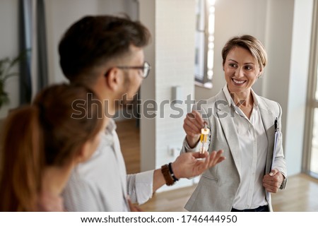 Happy real state agent giving new house key to a young couple.  Royalty-Free Stock Photo #1746444950
