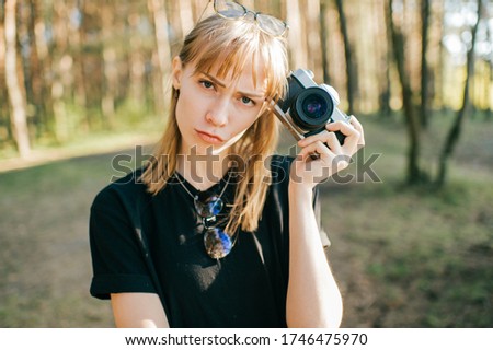 Portrait of beautiful young female photographer with short fair hair in black t-shirt stands with her camera.