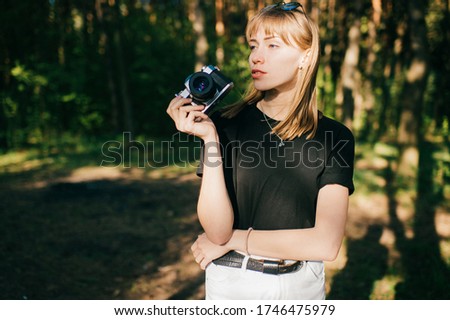 Portrait of beautiful young female photographer with short fair hair in black t-shirt stands with her camera.