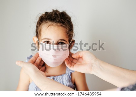 Girl with coronavirus mask prepared to go outside. Mother's hands putting the mask on her girl to prevent contagion