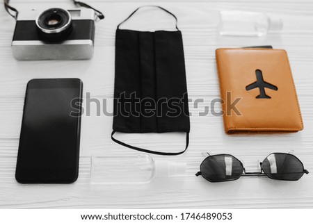 Safe travel in summer 2020. Black face mask, antiseptic and disinfectant, passport, sunglasses,photo camera, phone on white background. Coronavirus vacation, new normal